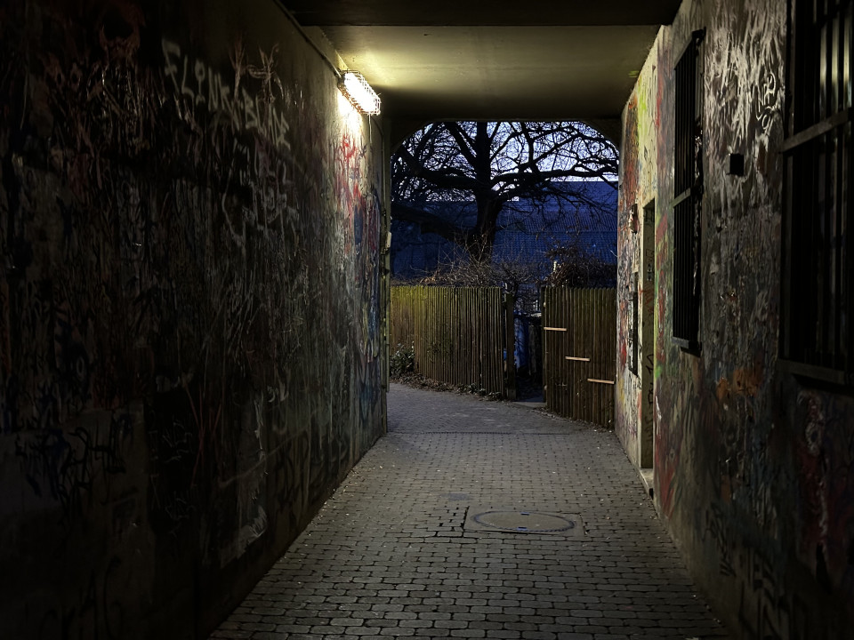 Dunkler Durchgang mit Graffiti an den Wänden und einem sichtbaren Ausgang am Ende.