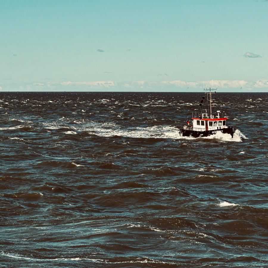 Ein Schlepper fährt durch die bewegte Nordsee vor Cuxhaven, umgeben von Wellen und Himmel.