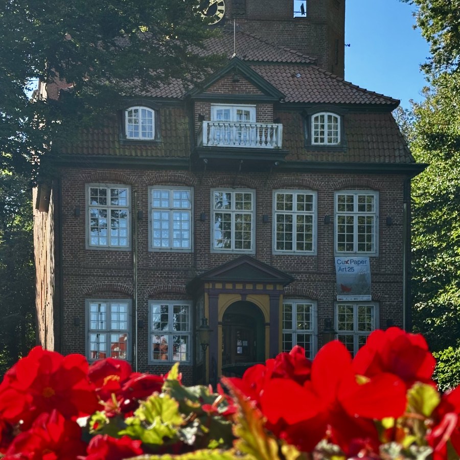 Schloss Ritzelbüttel in Cuxhaven umgeben von roten Blumen im Vordergrund.