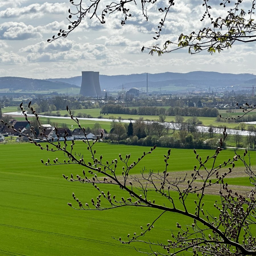 Blick auf eine grüne Landschaft mit einem Kühlturm und einem Fluss im Hintergrund, umgeben von Bäumen.